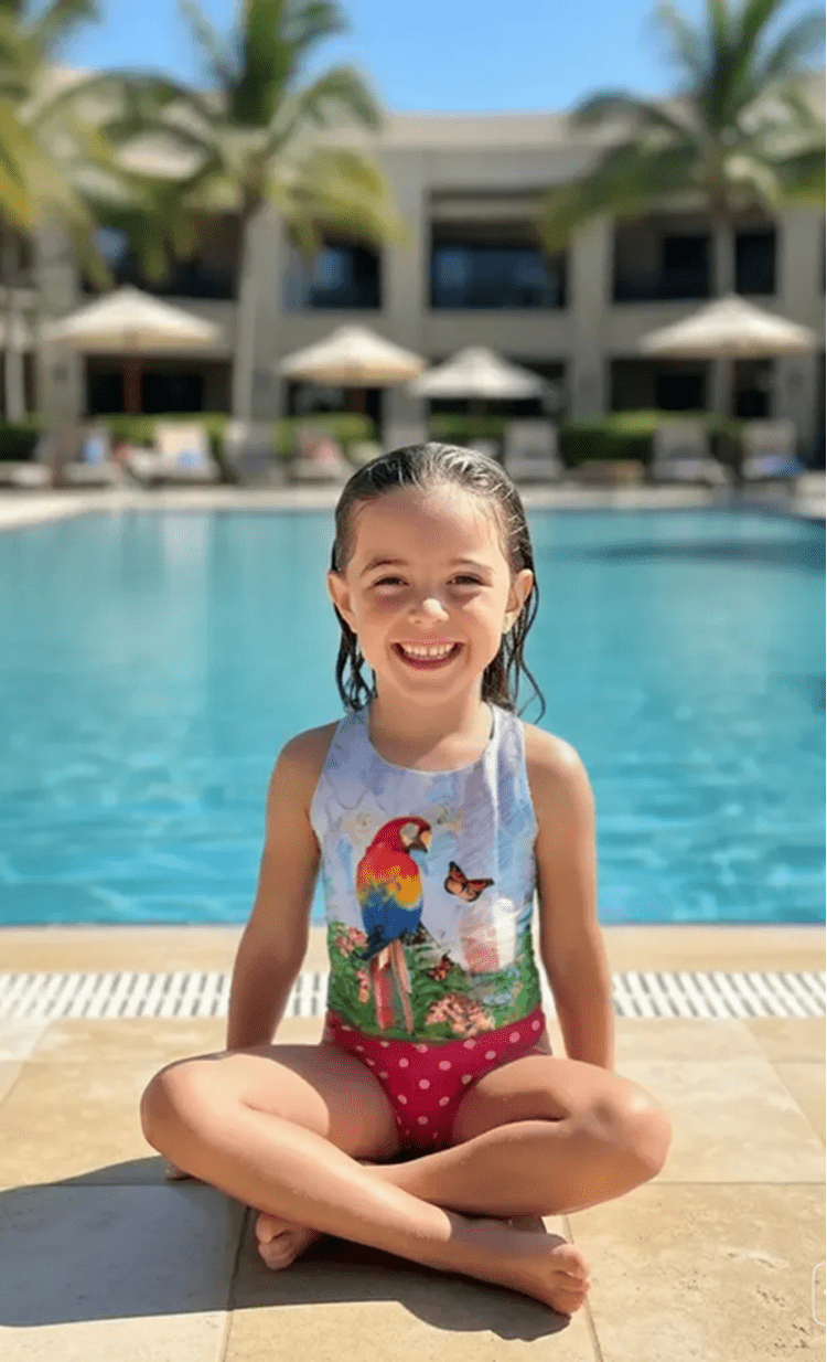 Parrots girls one-piece swimsuit with colourful tropical parrot print, model by pool, made in Canada