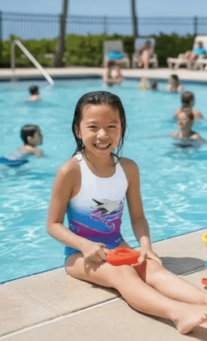 Dolphy girls one-piece swimsuit with purple dolphin print, model by pool, made in Canada