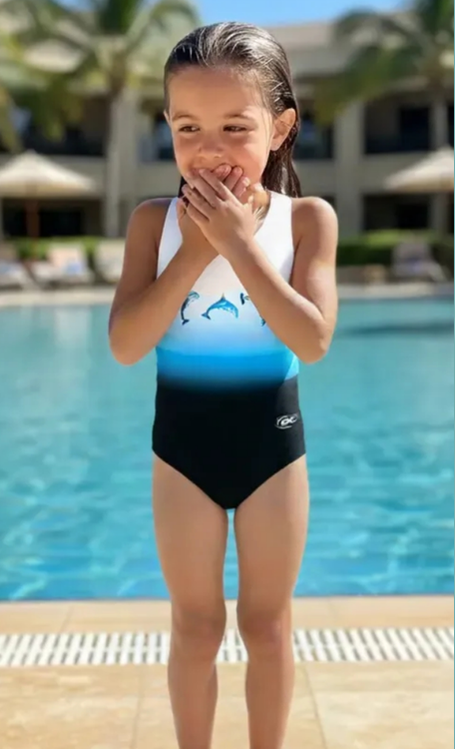 Child wearing a two-tone swimsuit with a dolphin design by a pool.