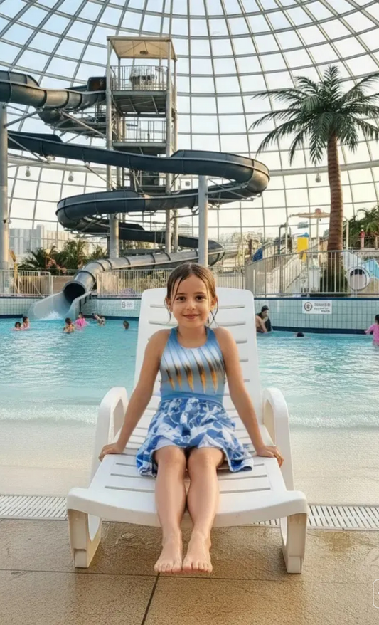 Child sitting on a lounge chair by an indoor pool with a water slide in the background