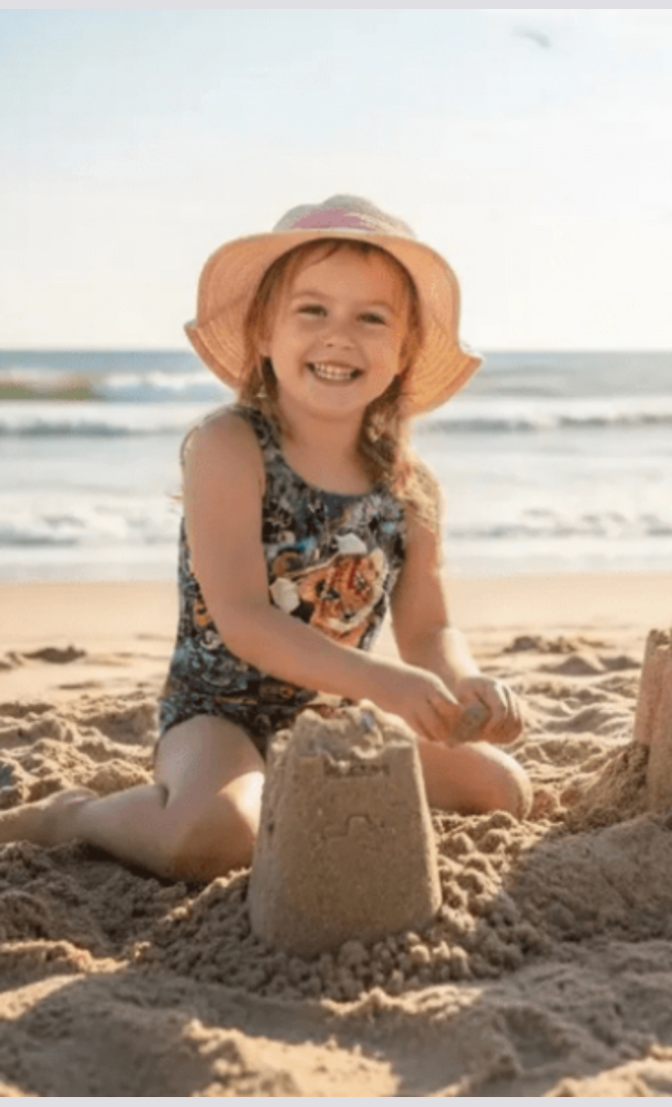 Wildlife girls one-piece swimsuit with cute baby tiger print, model on beach, made in Canada